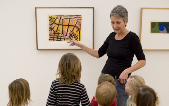Uma mulher explica um quadro a um grupo de crianças
