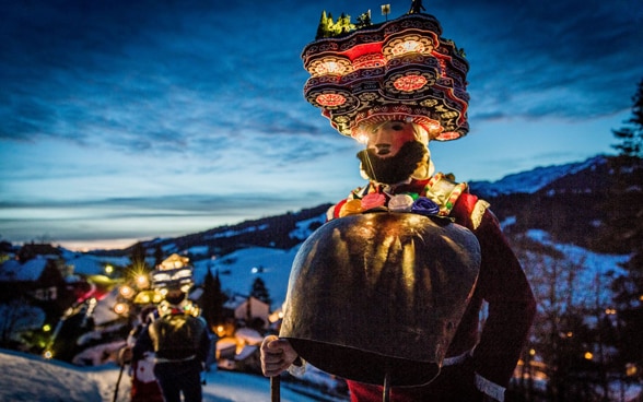 傍晚时分，化装戴面具的男人们行走在冬季山野中。