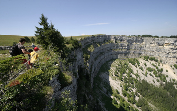 A family peers over the steep rock face of the Creux de Van (canton of Neuchâtel).