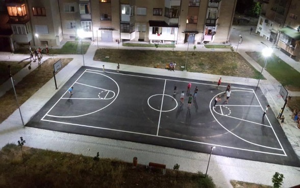 : A group of young people playing on a floodlit basketball court.