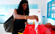 Une jeune femme insère un bulletin de vote plié dans une urne.