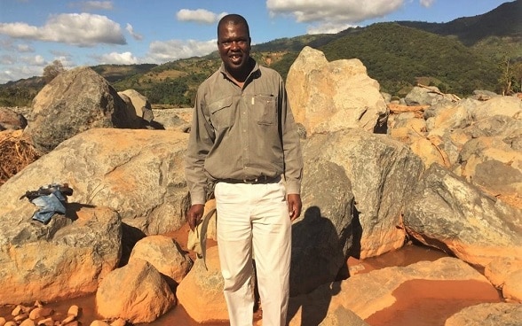 Edson Mugore, Programme Office with the Swiss Agency for Development and Cooperation standing amid the boulders that came on top of houses in Chimanimani in Zimbabwe. Houses and many family possessions were destroyed by Cyclone Idai in March 2019. 