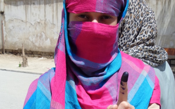 Eine Wählerin zeigt vor einem Wahlbüro ihren tintengefärbten Finger.