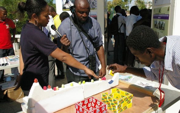 A female Haitian engineer employed by the SDC answers a journalist's questions at a stand.