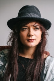 Die albanische Musikerin Elina Duni sitzt auf einem Stuhl. Sie trägt einen Hut.