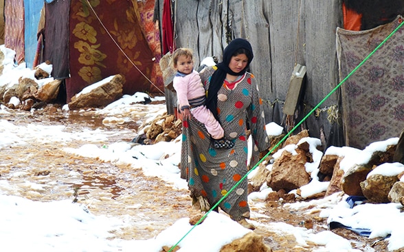 Une femme porte un enfant dans ses bras dans un camp de réfugiés syrien.