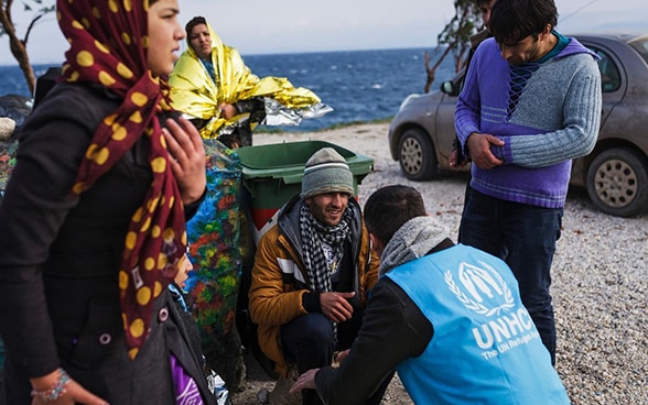 Ein Mitarbeiter des UNHCR empfängt Flüchtlinge an einem Strand.