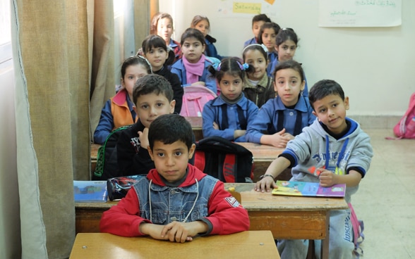 Eine Gruppe von Mädchen und Buben sitzen dicht gedrängt an Pulten in einem Schulzimmer.