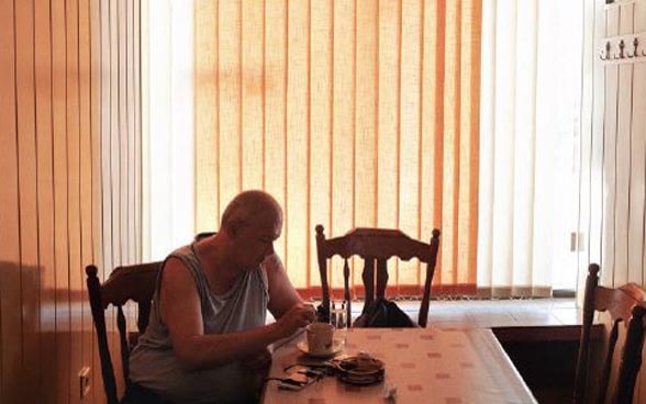  Un homme âgé est assis seul à une table dans une pièce sombre.