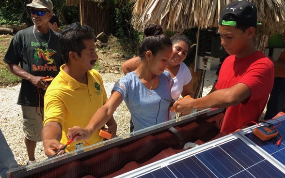 Mujeres y hombres de la comunidad ante un techo con paneles solares reciben una introducción en cuanto a su utilización.