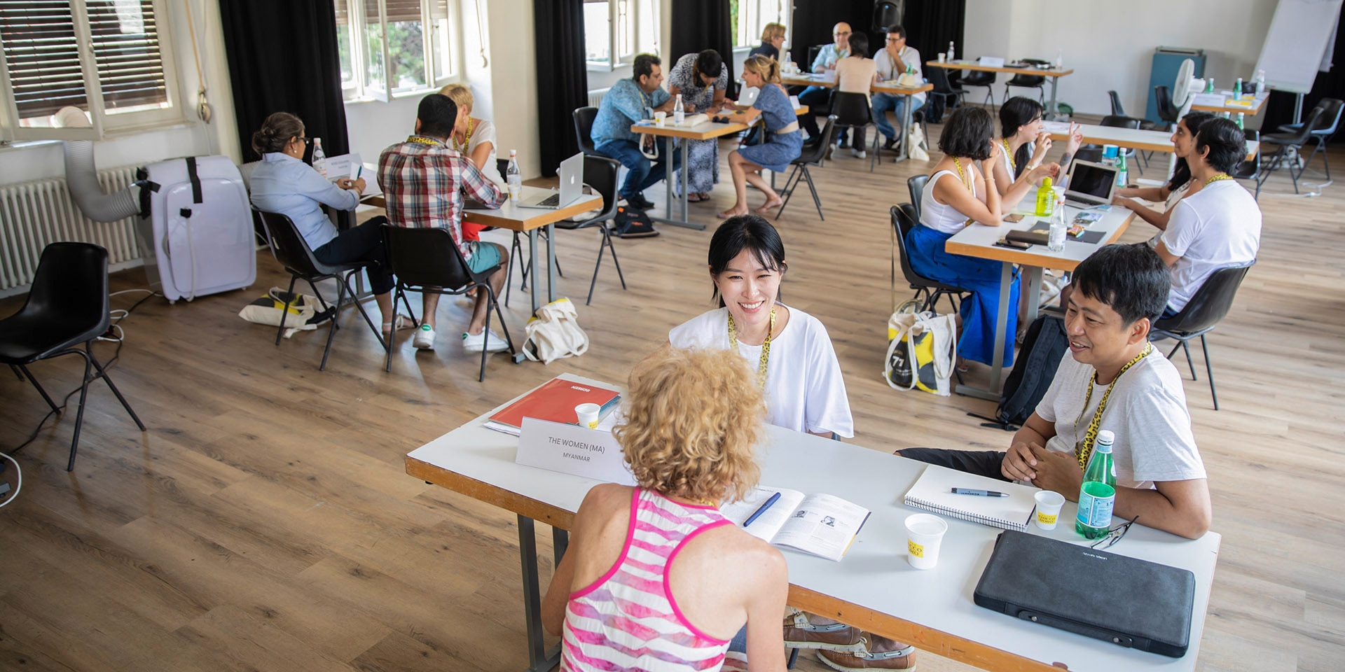 En una sala algunos jóvenes trabajan en grupo, sentados alrededor de mesas.