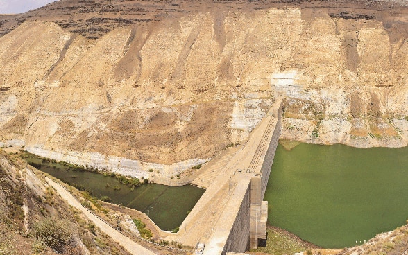 Wasser fliesst auf beiden Seiten eines Staudamms, der sich zwischen zwei Berghängen erhebt.