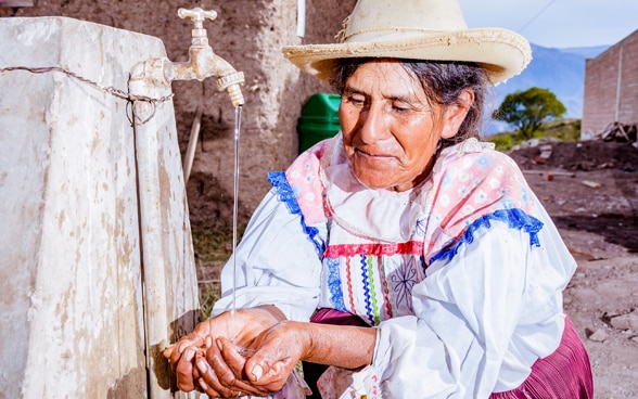 Eine Bolivianerin wäscht sich an einem Wasserhahn die Hände.