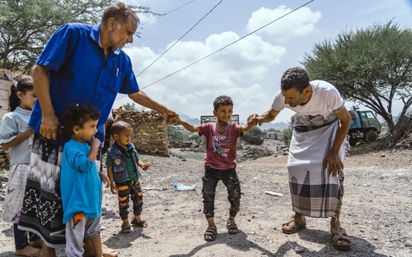 Two men hold a child by the hand because he cannot walk alone.