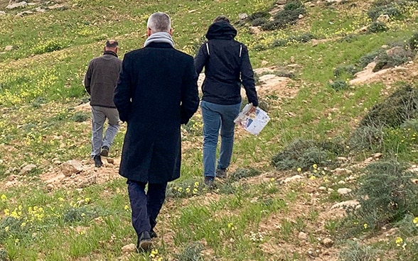 Simon Geissbühler, from behind, walks through the hills of Masafer Yatta behind two other local people.