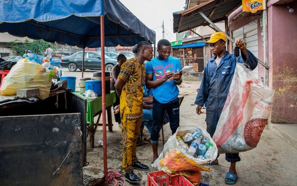 En la metrópolis nigeriana de Lagos algunos hombres pesan los envases de plástico recolectados y registran su peso en el punto de reciclaje.