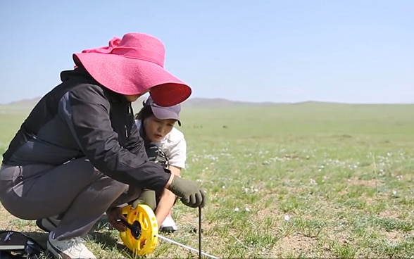 Two women taking measurements in a field.
