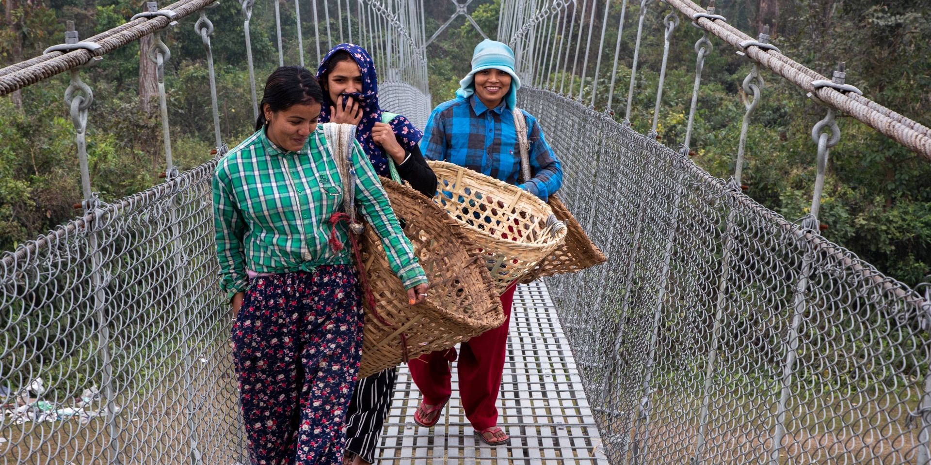 Three smiling women cross a bridge in Nepal.