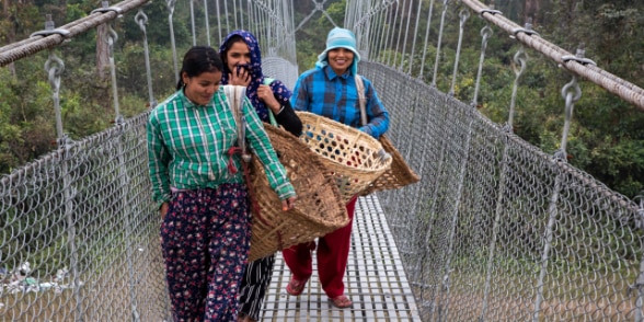 Trois femmes traversent un pont népalais en souriant