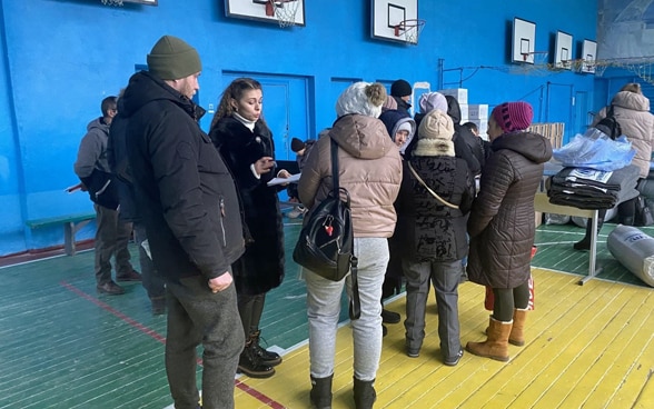 Une femme accueille des personnes qui arrivent dans un gymnase transformé en abri d’urgence. 