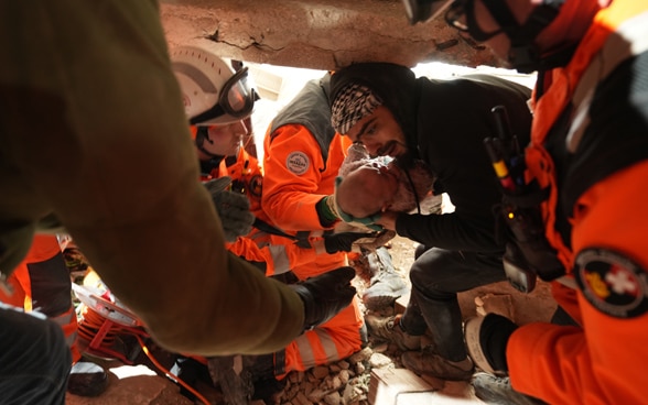  A man, surrounded by members of Swiss Rescue, cradling a four-month-old girl who has just been rescued from a fallen building.