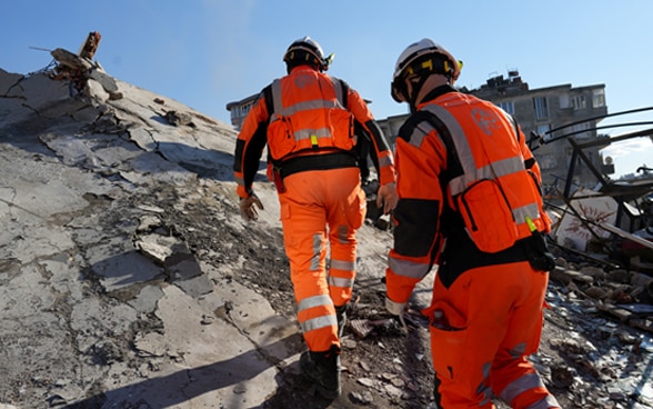  Due membri della Catena di salvataggio camminano sui resti di una casa crollata.