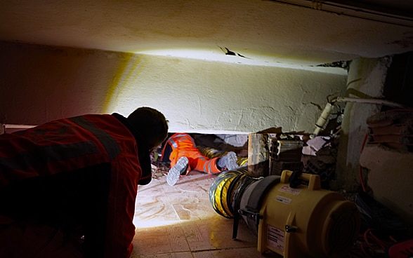 Ein Mitglied der Rettungskette kriecht unter Trümmern eines Hauses. Ein Scheinwerfer gibt ihm Licht.