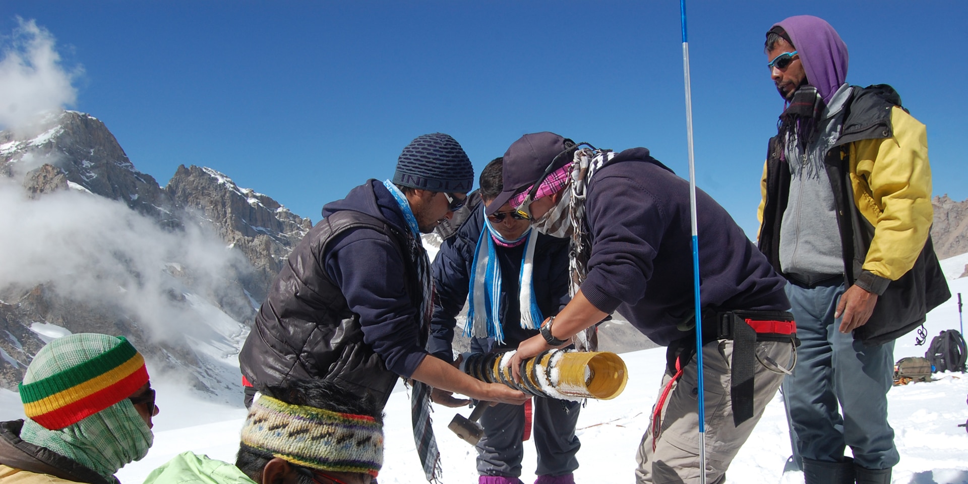 Seven men on a glacier in the mountains making scientific measurements in the snow.