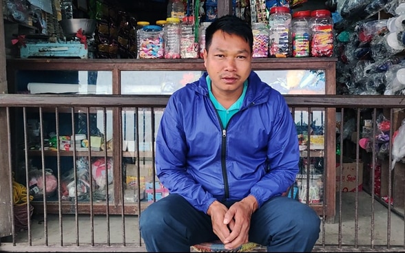 A shopkeeper sits in front of his shop.