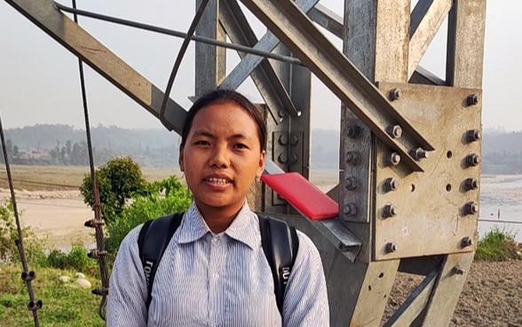 Une élève népalaise se tient sur le pont suspendu.