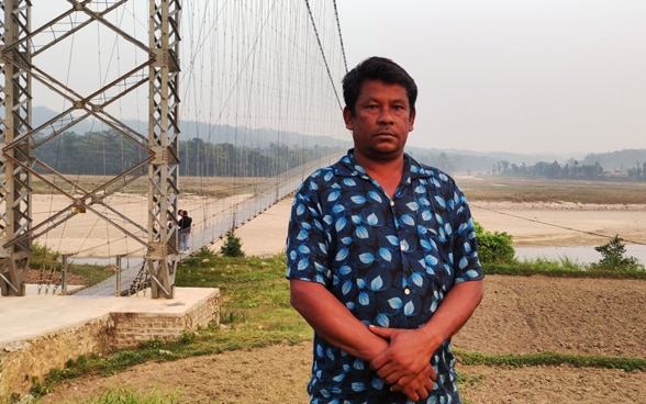 A man stands in front of the suspension bridge.
