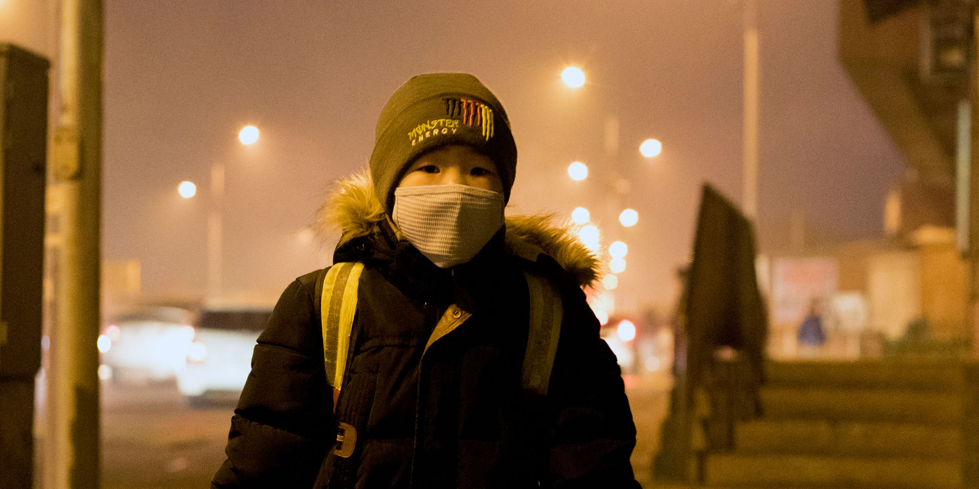 Ein Junge mit einem Schulrucksack und einer Gesichtsmaske wartet an einer Bushaltestelle in Ulaanbaatar.