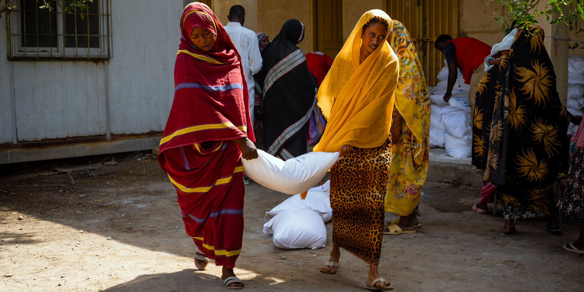 Two women carrying a bag of grains.