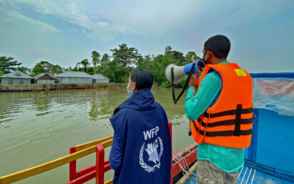 Un miembro del personal del PMA y su compañera en una barca informan por megáfono a las comunidades afectadas por las inundaciones en Bangladesh.