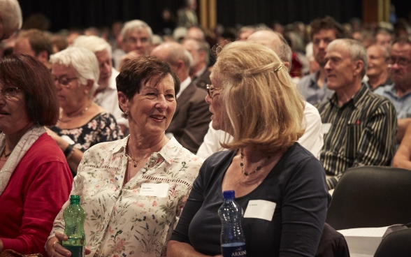 Deux participantes assises parmi le public de la conférence annuelle parlent ensemble de façon animée.