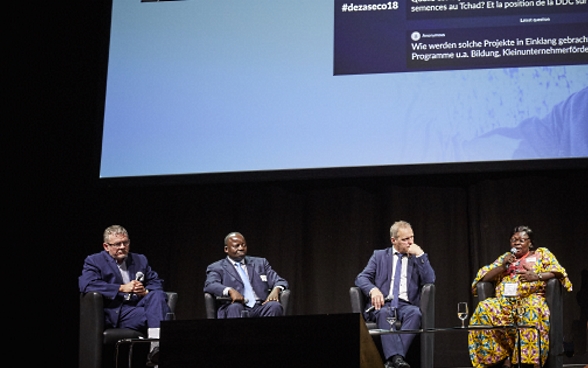 Mansour N’Diaye, Dominique Guenat, Pierre-André Page, Mariane Nguerassem und die Moderatorin Melanie Pfändler sitzen auf der Bühne. Im Hintergrund sieht man die Power Point auf der Publikumsfragen eingeblendet sind.