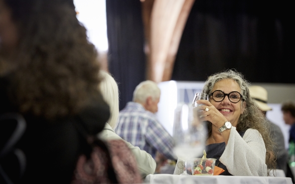 11.	A participant at a standing table holding a glass of water and smiling.