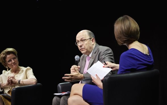 Marie-Gabrielle Ineichen-Fleisch et Melanie Pfändler sont assises sur la scène et écoutent attentivement Thomas Gass qui est assis entre elles et parle dans le microphone.