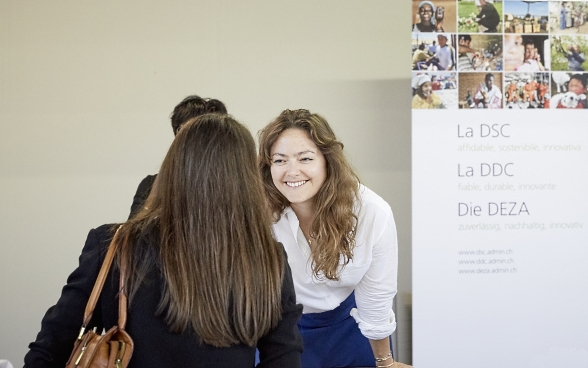 A participant talking to a stand supervisor at the SDC/SECO stand. There is an SDC poster in the background.