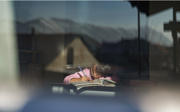 A girl sitting at a table, writing.