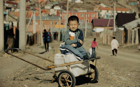 A boy sitting on a handcart, with his eyes closed.