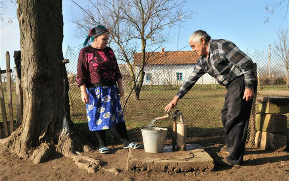 Zwei Menschen füllen einen Eimer mit Wasser von einem öffentlichen Wasserhahn