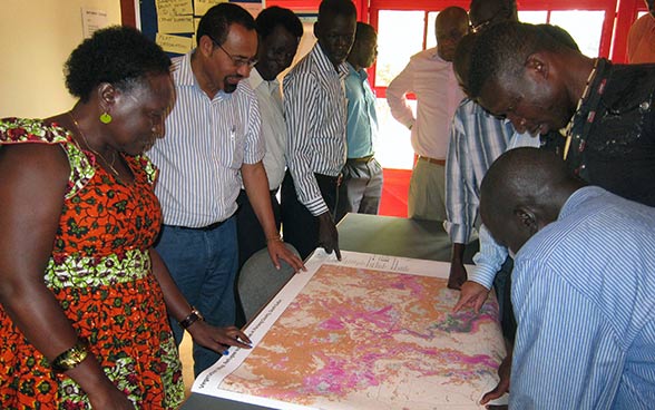 A group of people standing around a table with a map spread over it.