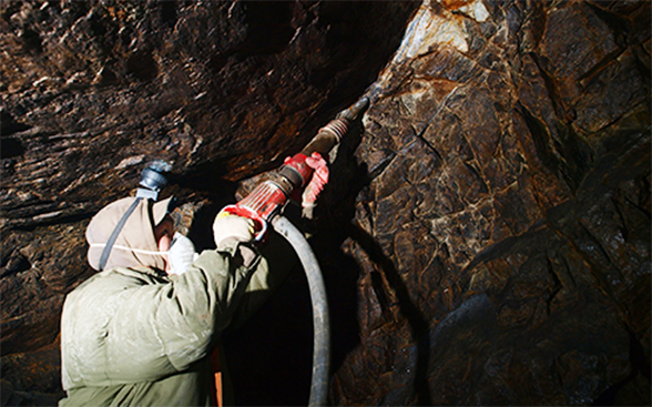 A miner is drilling rock in search of gold