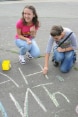 Six young people in a circle drawing on the ground with chalk.