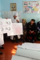 Three women in white coats use posters to present information on breastfeeding to a group of women.