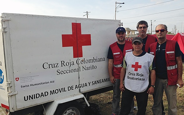Tre membri del Corpo svizzero d’aiuto umanitario e un collaboratore della Croce rossa ecuadoriana in posa davanti a un rimorchio impiegato per trasportare acqua potabile. 