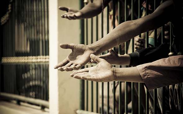 Mains tendues à travers les barreaux d’une cellule de prison.