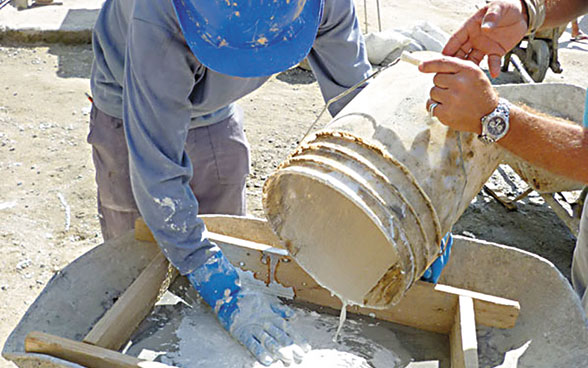 Two workers pour cement into a wooden mould.
