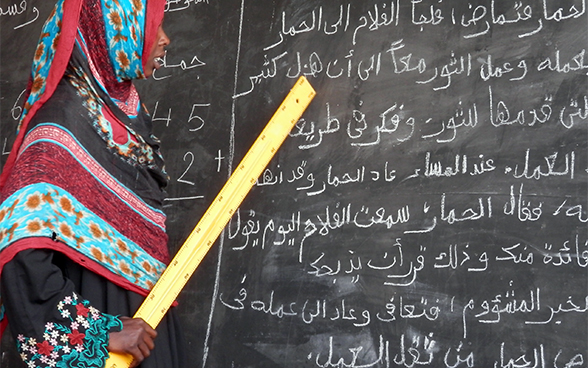 Une jeune mère, tenant une règle dans la main et lisant ce qui est écrit sur le tableau noir, bénéficie de l’apprentissage dans un centre d’alphabétisation à Oum Hadjer, dans la région du Batha, au Tchad. 